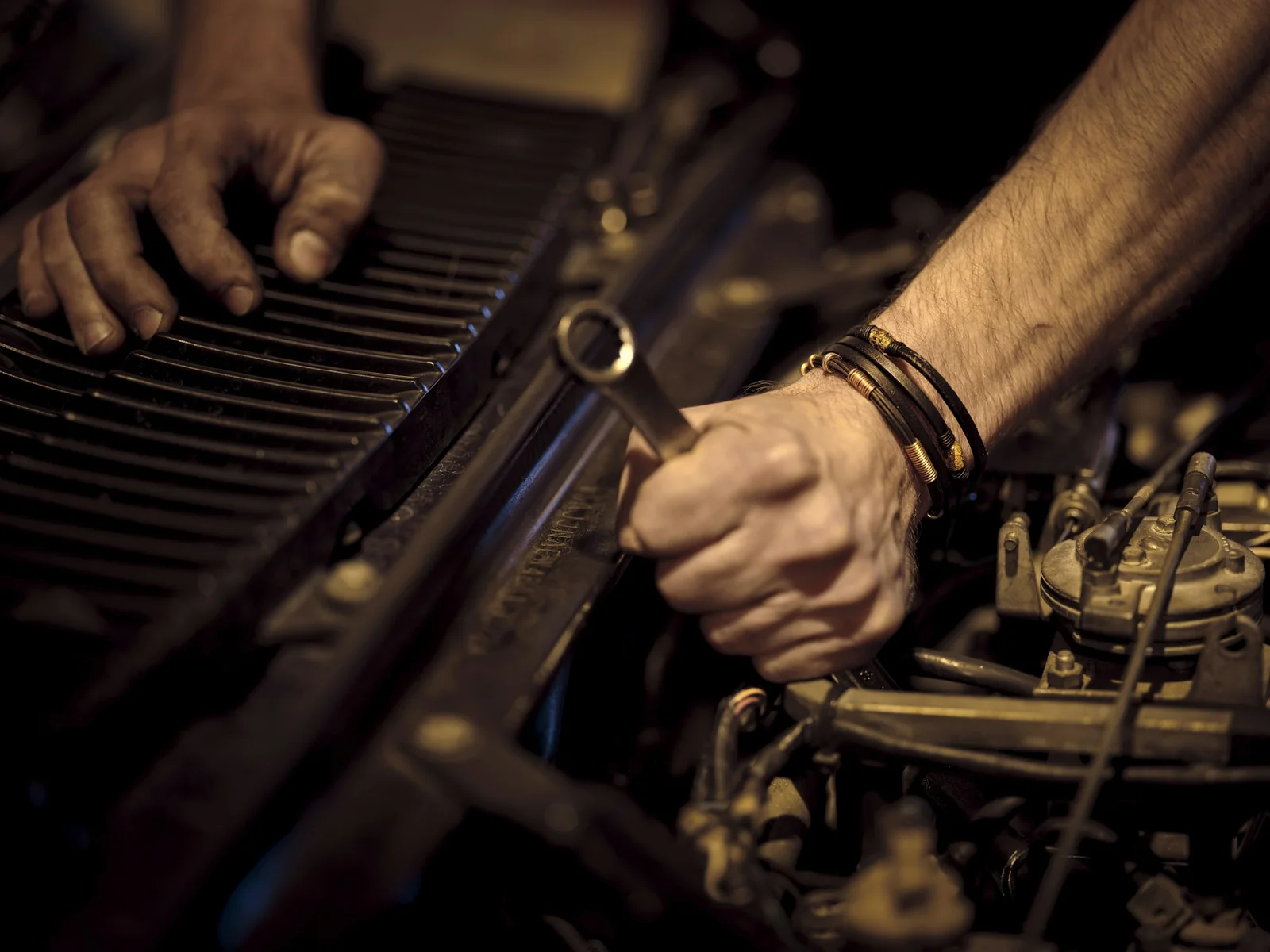 A mechanic's hands holding a wrench over an engine.